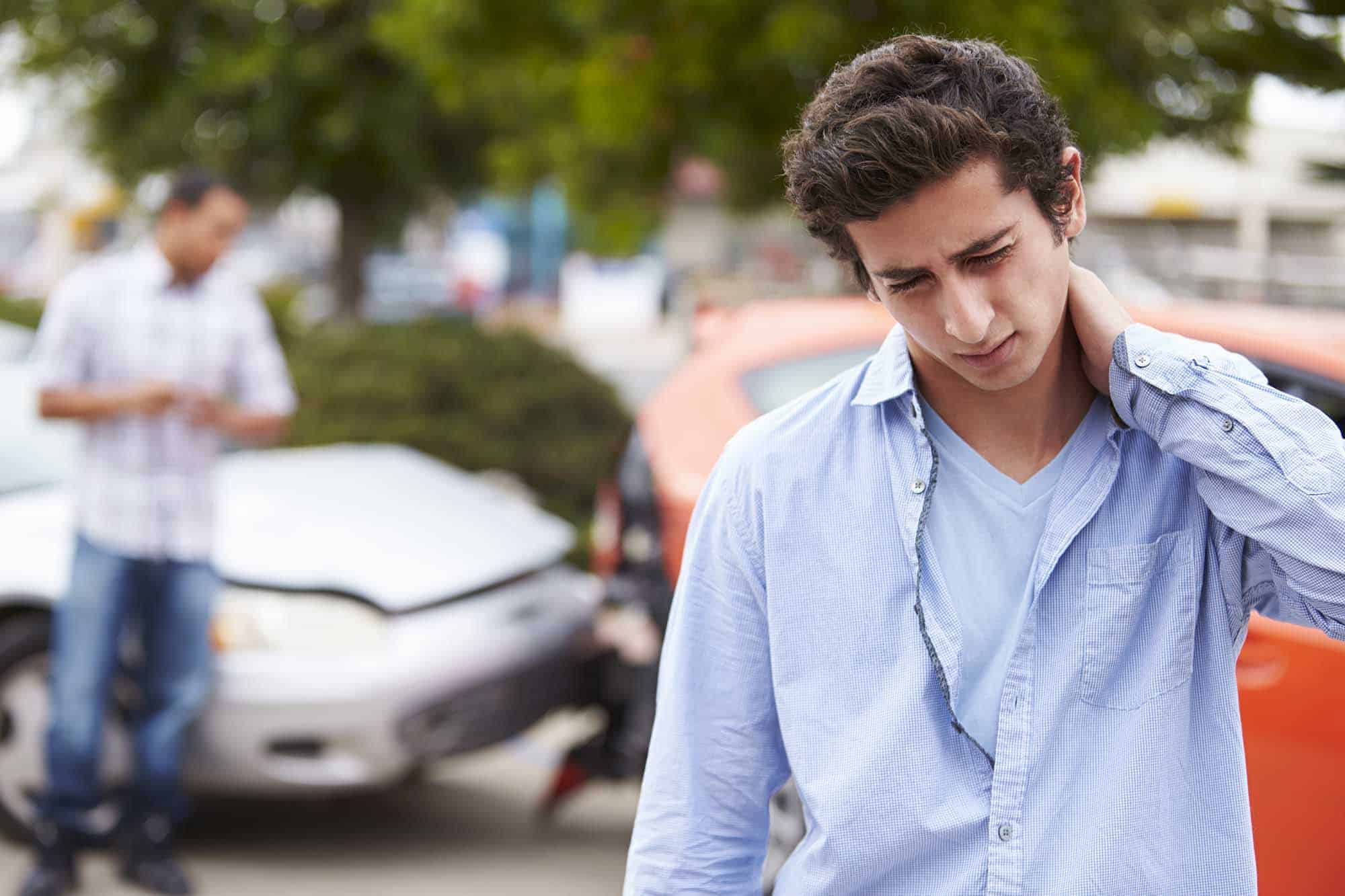 Auto-Accident-Injury A man with a neck injury in front of a car.