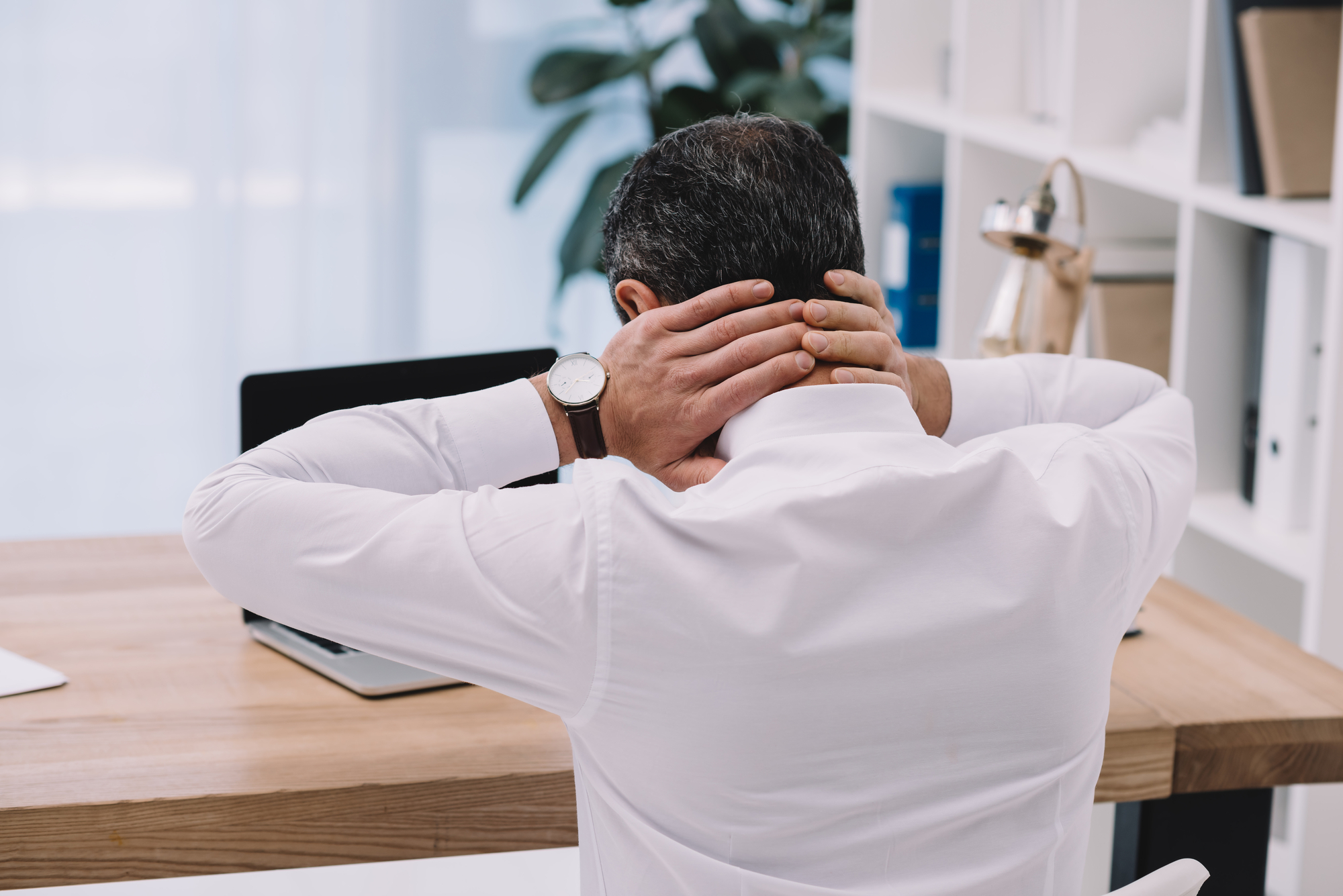 A man is sitting at a desk with his hands on his head.
