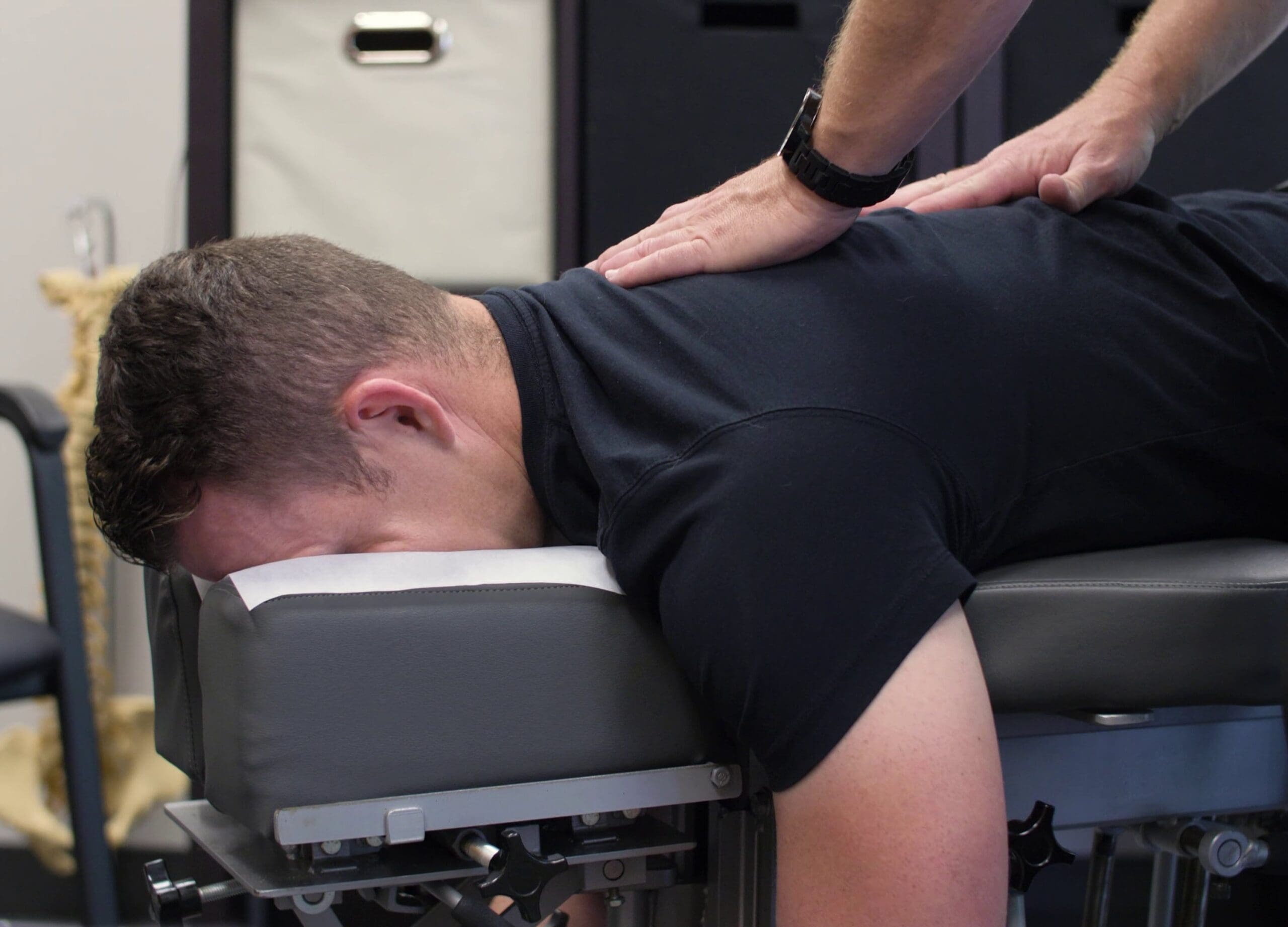 A chiropractor performs a spinal adjustment on a male patient lying face-down on a treatment table.